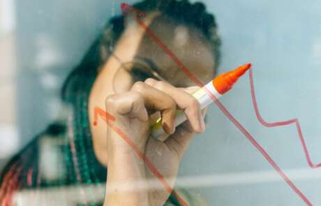 Woman drawing on window with red marker, drawing a stock market arrow graph