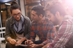 People, friends and discussion with tablet at cafe on project, deadline or schedule at indoor restaurant. Group of students on technology for online browsing, research or communication at coffee shop